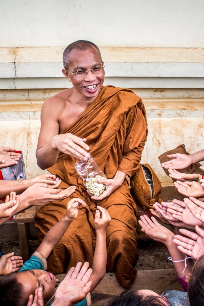 Smiling monk shares food with eager children in an Asian community gathering.