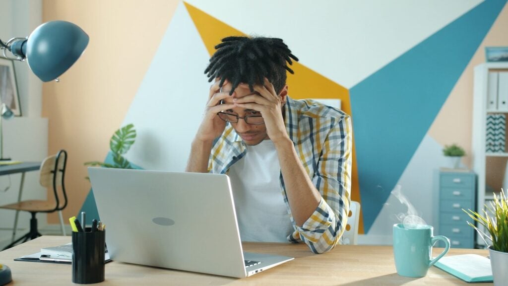 Man holding head in frustration at desk with laptop.