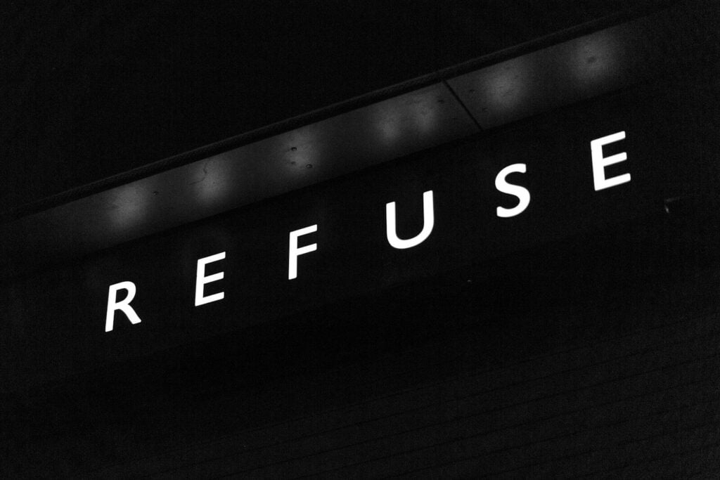 A black and white sign with the word REFUSE in illuminated capital letters